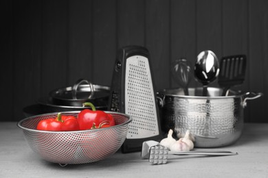 Photo of Dishware, cooking utensils, vegetables and garlic on grey wooden table