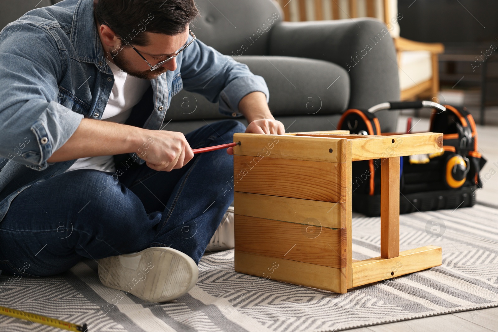 Photo of Man repairing wooden stool with screwdriver at home