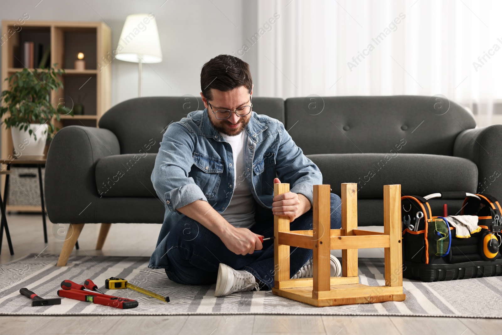 Photo of Man repairing wooden stool with screwdriver at home