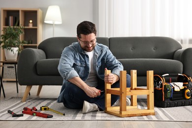 Photo of Man repairing wooden stool with screwdriver at home