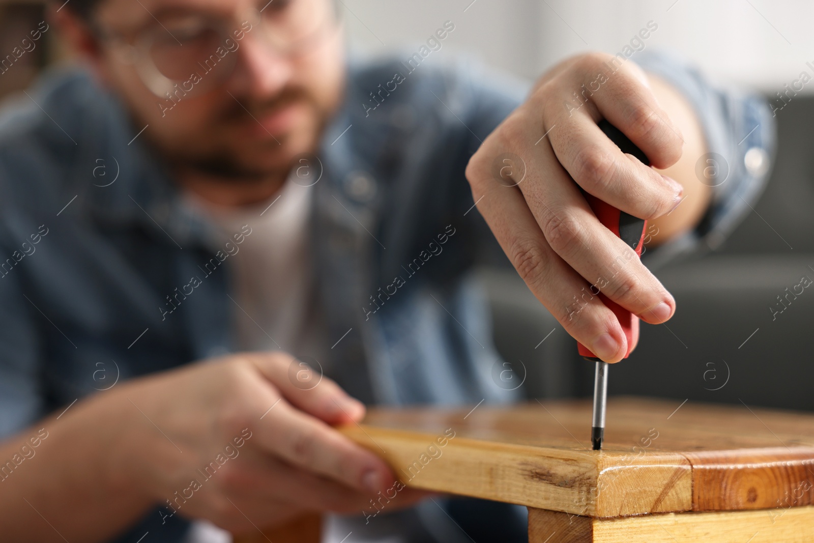 Photo of Man repairing wooden stool with screwdriver at home, selective focus