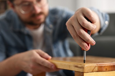 Photo of Man repairing wooden stool with screwdriver at home, selective focus