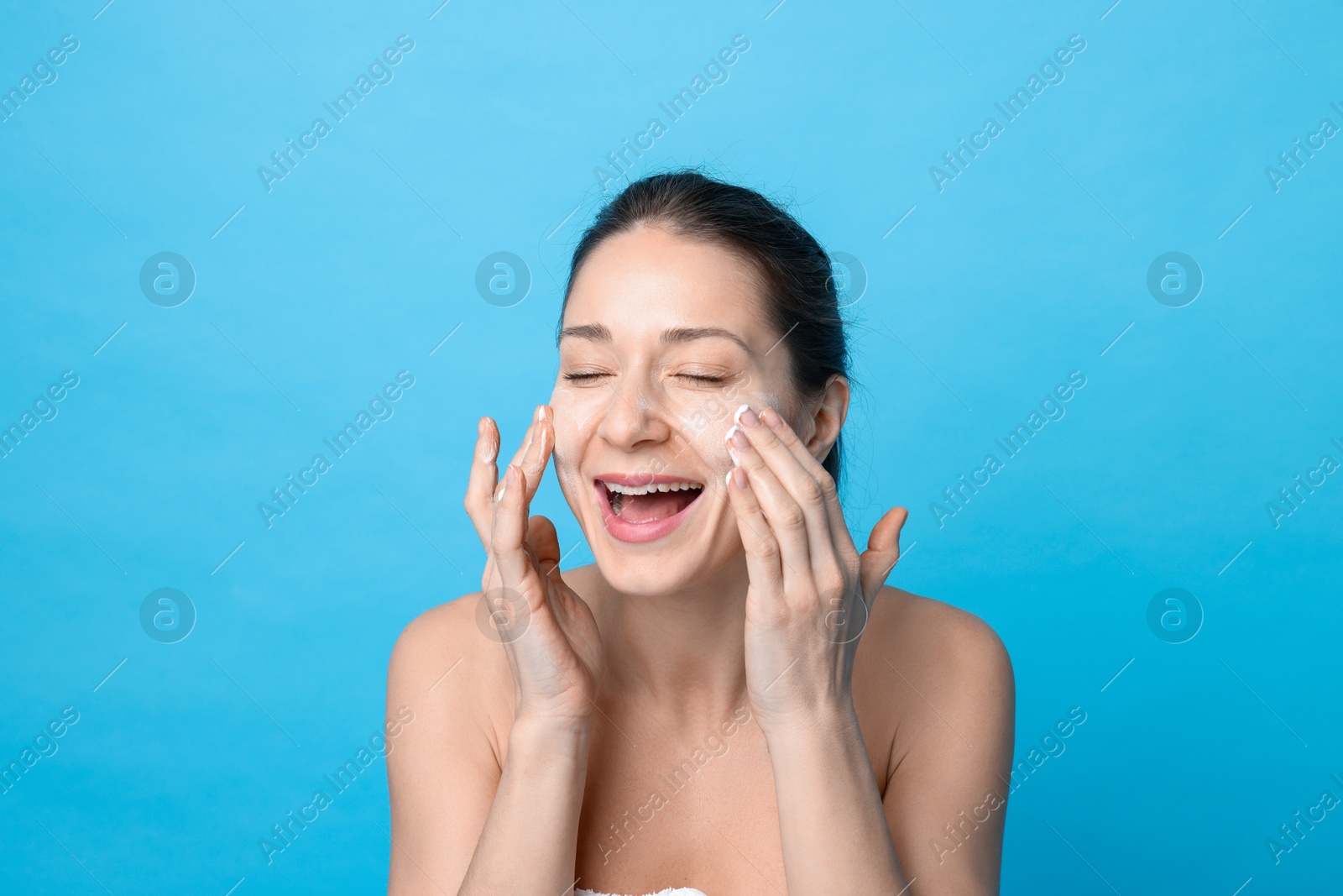 Photo of Spa day. Happy woman applying mask onto her face on light blue background