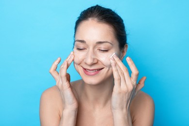 Photo of Spa day. Happy woman applying mask onto her face on light blue background