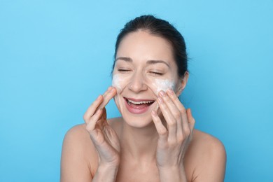 Photo of Spa day. Happy woman applying mask onto her face on light blue background