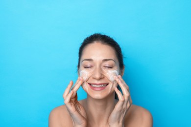 Photo of Spa day. Happy woman applying mask onto her face on light blue background