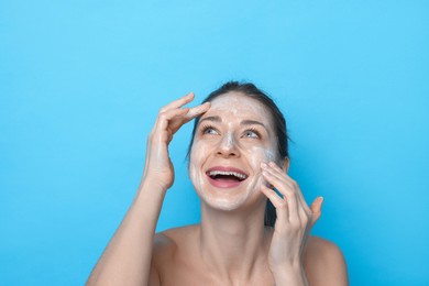 Photo of Spa day. Happy woman applying mask onto her face on light blue background