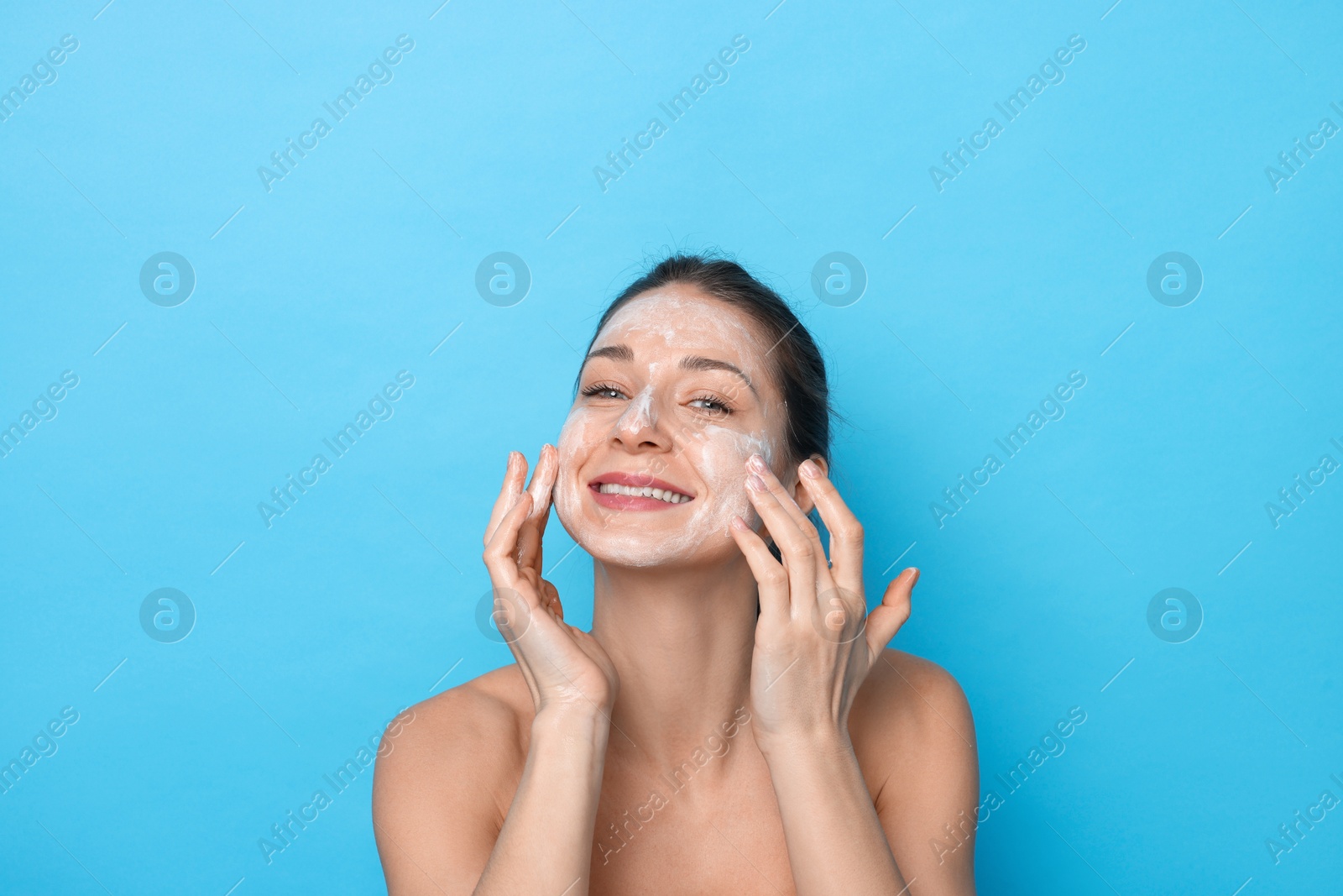 Photo of Spa day. Happy woman applying mask onto her face on light blue background