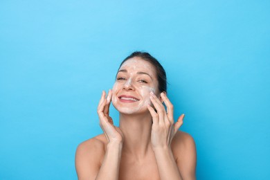 Photo of Spa day. Happy woman applying mask onto her face on light blue background