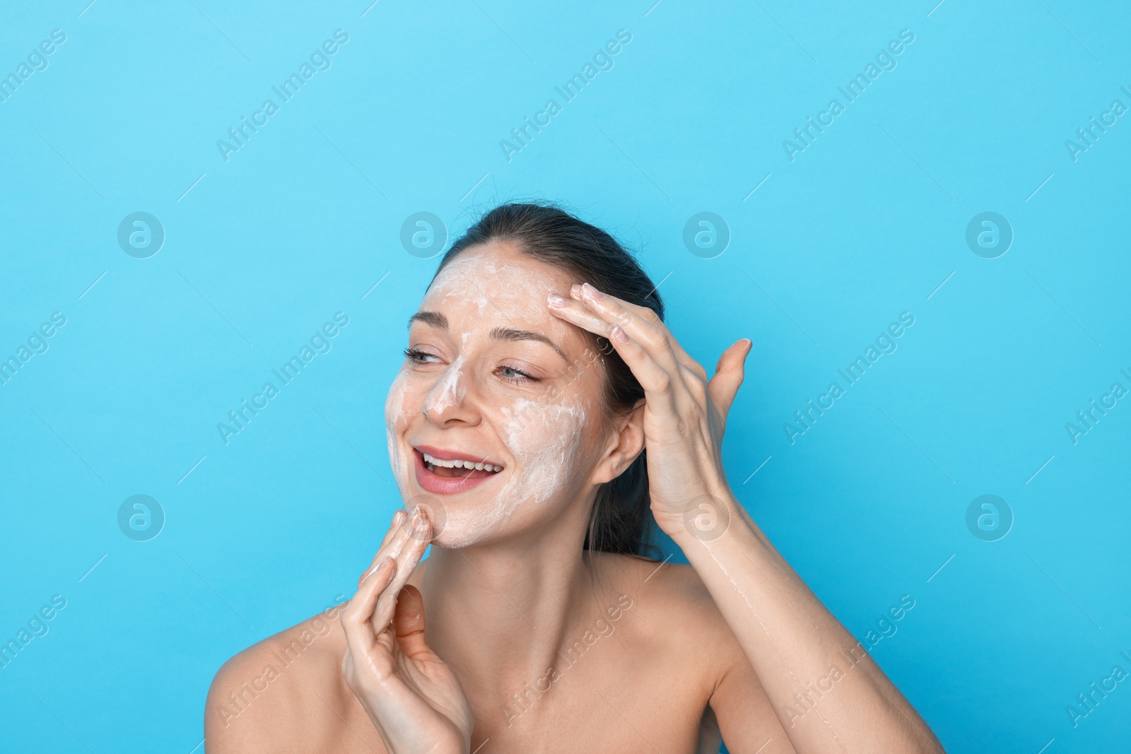 Photo of Spa day. Happy woman applying mask onto her face on light blue background