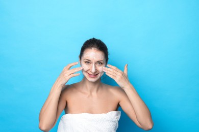 Photo of Spa day. Happy woman applying mask onto her face on light blue background