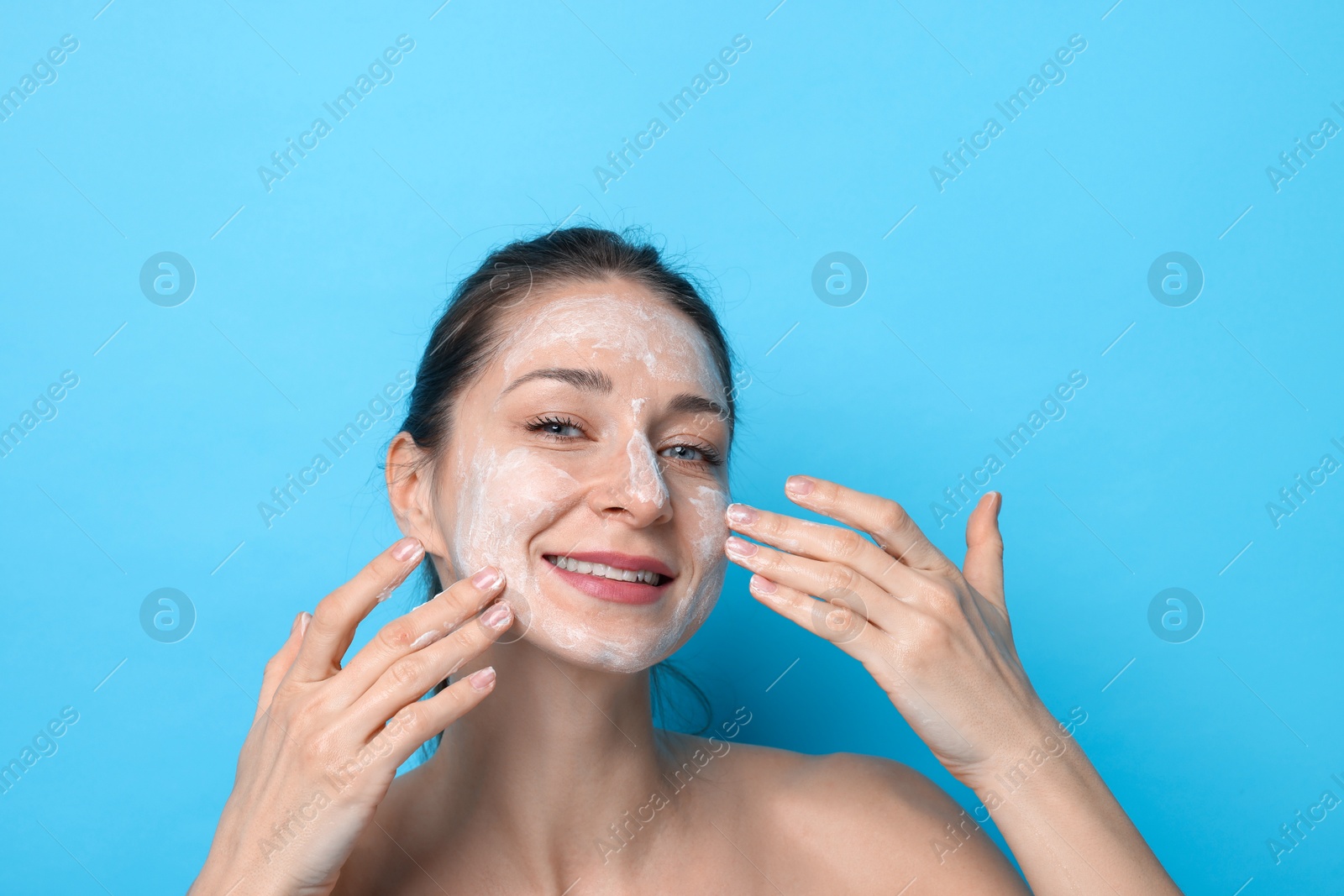 Photo of Spa day. Happy woman applying mask onto her face on light blue background