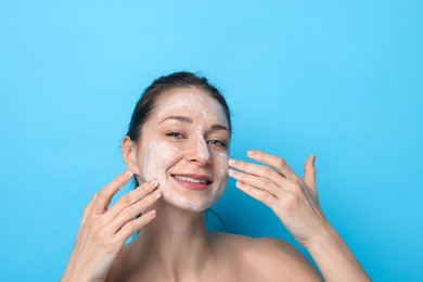 Photo of Spa day. Happy woman applying mask onto her face on light blue background