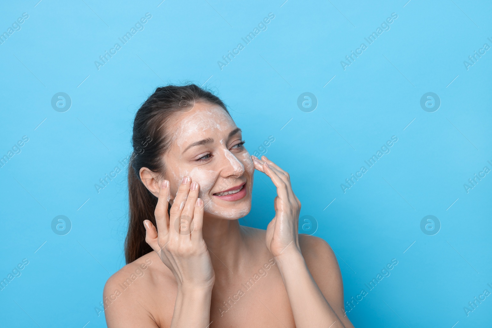 Photo of Spa day. Happy woman applying mask onto her face on light blue background