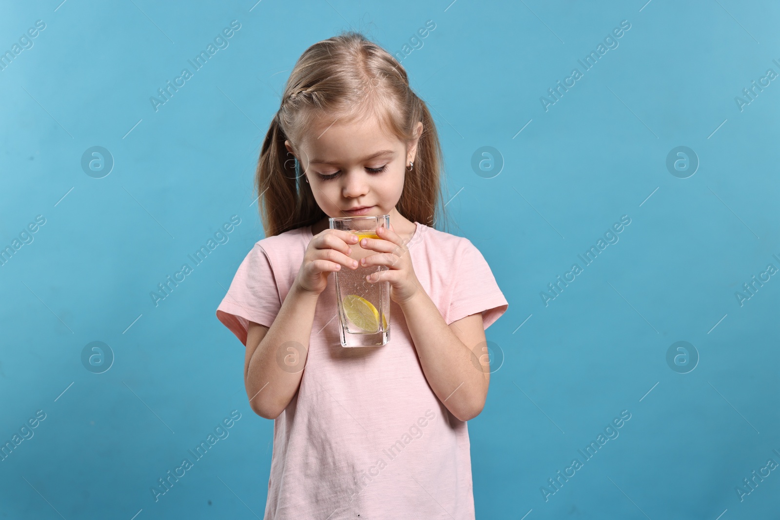 Photo of Girl with glass of lemonade on light blue background. Refreshing drink