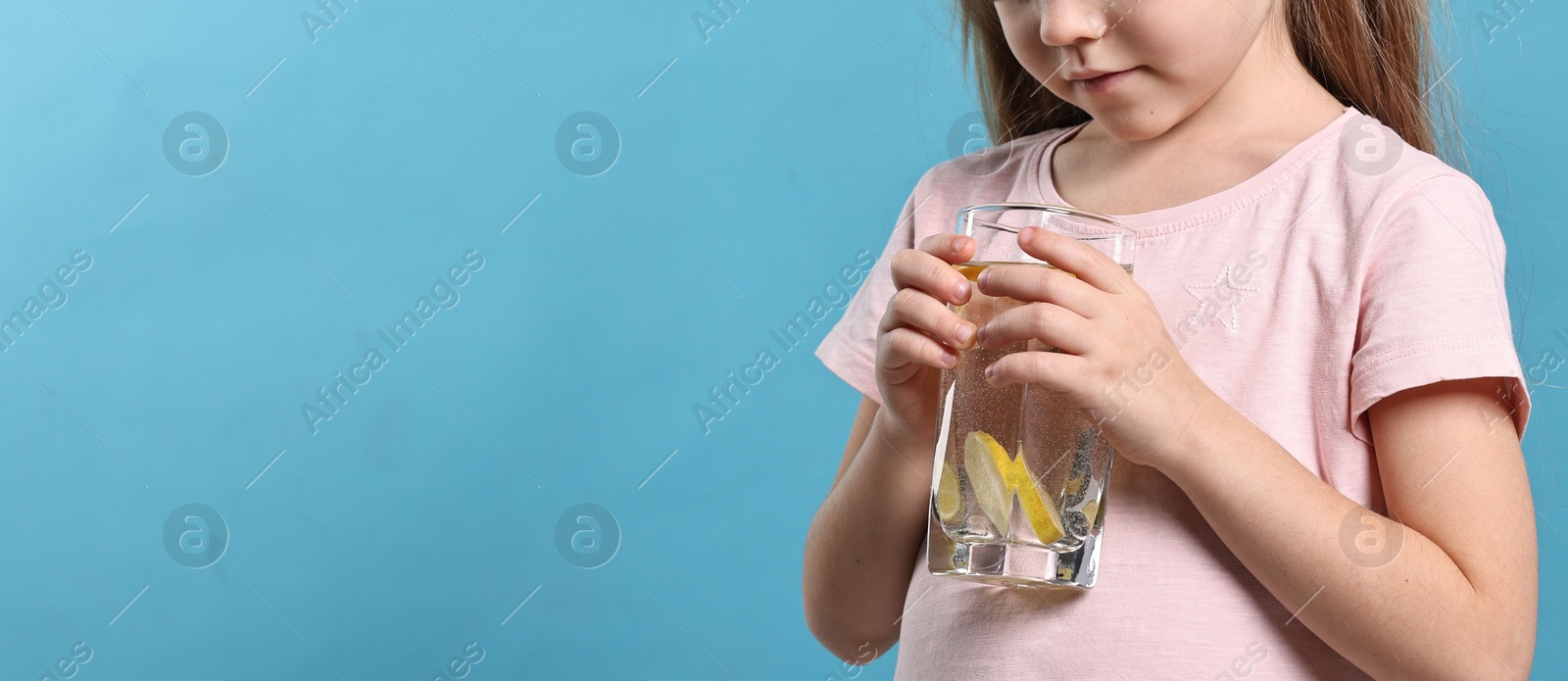 Photo of Girl with glass of lemonade on light blue background, closeup and space for text. Refreshing drink