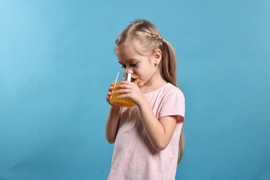 Photo of Girl drinking tasty orange juice on light blue background. Refreshing drink