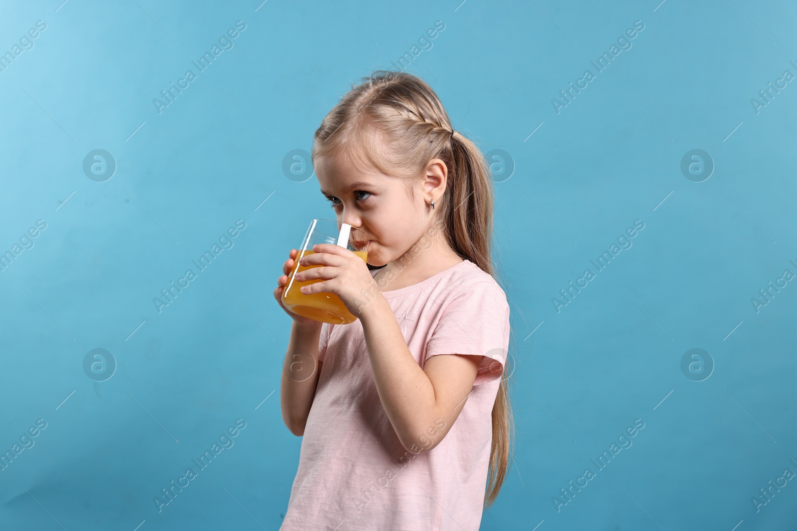 Photo of Girl drinking tasty orange juice on light blue background. Refreshing drink