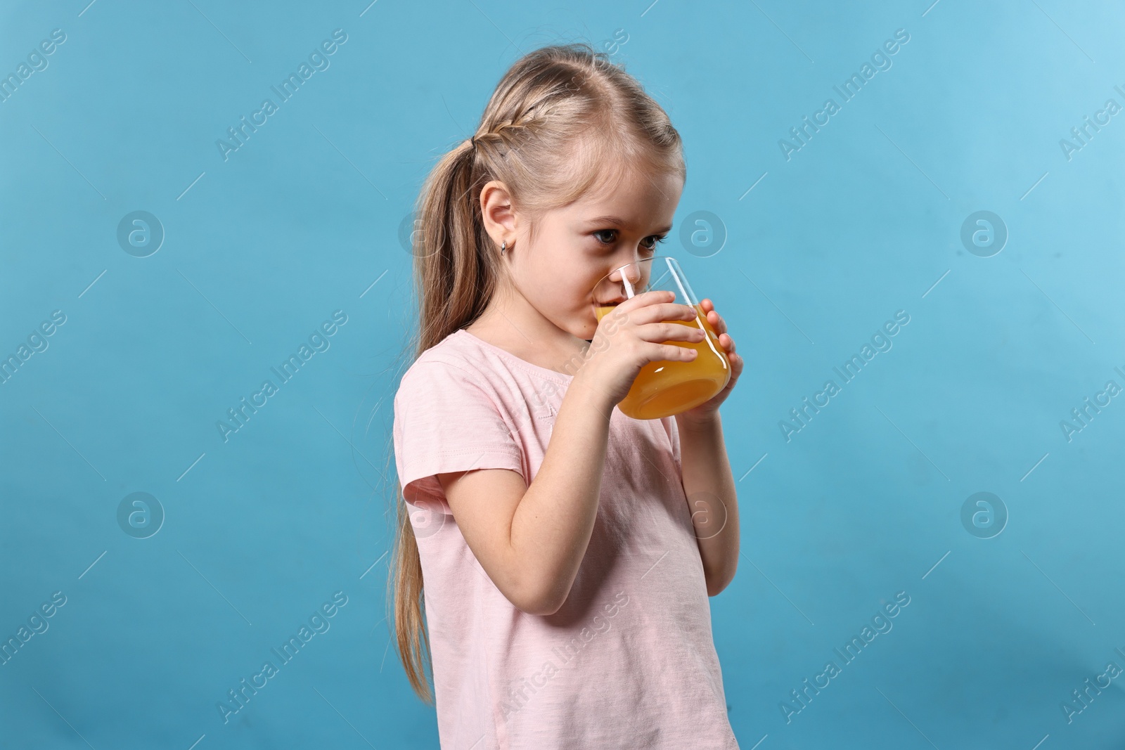 Photo of Girl drinking tasty orange juice on light blue background. Refreshing drink