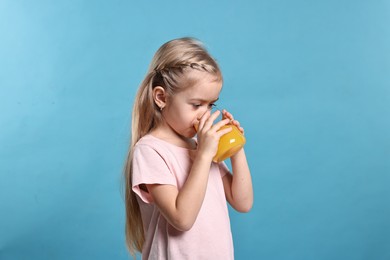 Photo of Girl drinking tasty orange juice on light blue background. Refreshing drink