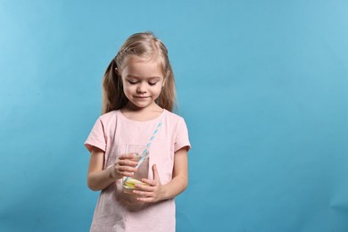 Photo of Girl with glass of lemonade on light blue background, space for text. Refreshing drink