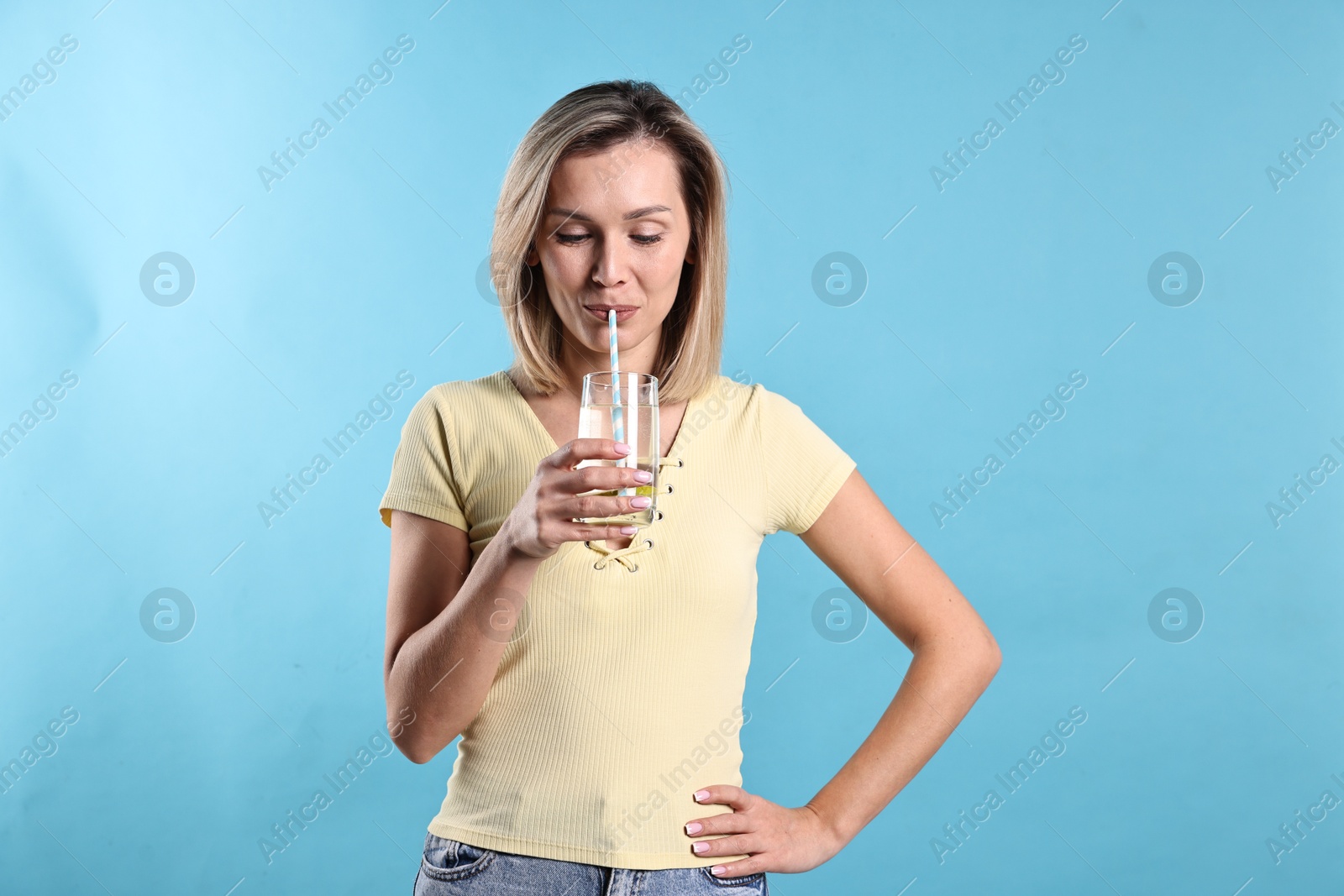 Photo of Woman drinking tasty lemonade on light blue background. Refreshing drink