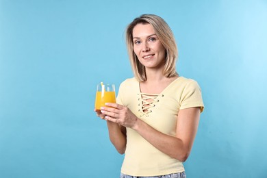 Photo of Woman with glass of orange juice on light blue background, space for text. Refreshing drink