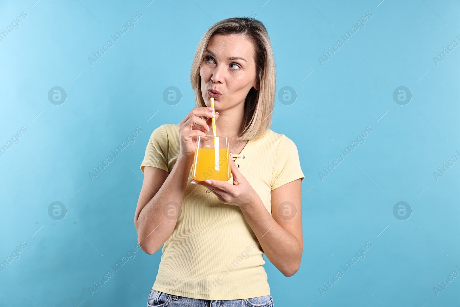 Photo of Woman drinking tasty orange juice on light blue background. Refreshing drink