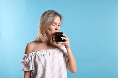 Photo of Woman drinking tasty refreshing soda drink on light blue background