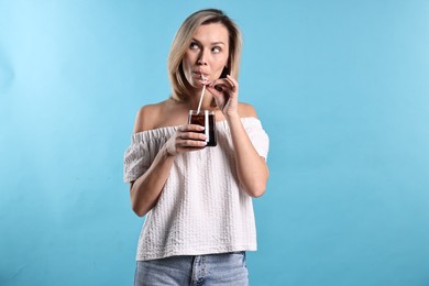 Photo of Woman drinking tasty refreshing soda drink on light blue background