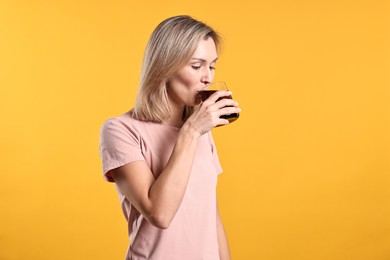 Photo of Woman drinking tasty refreshing soda drink on orange background.