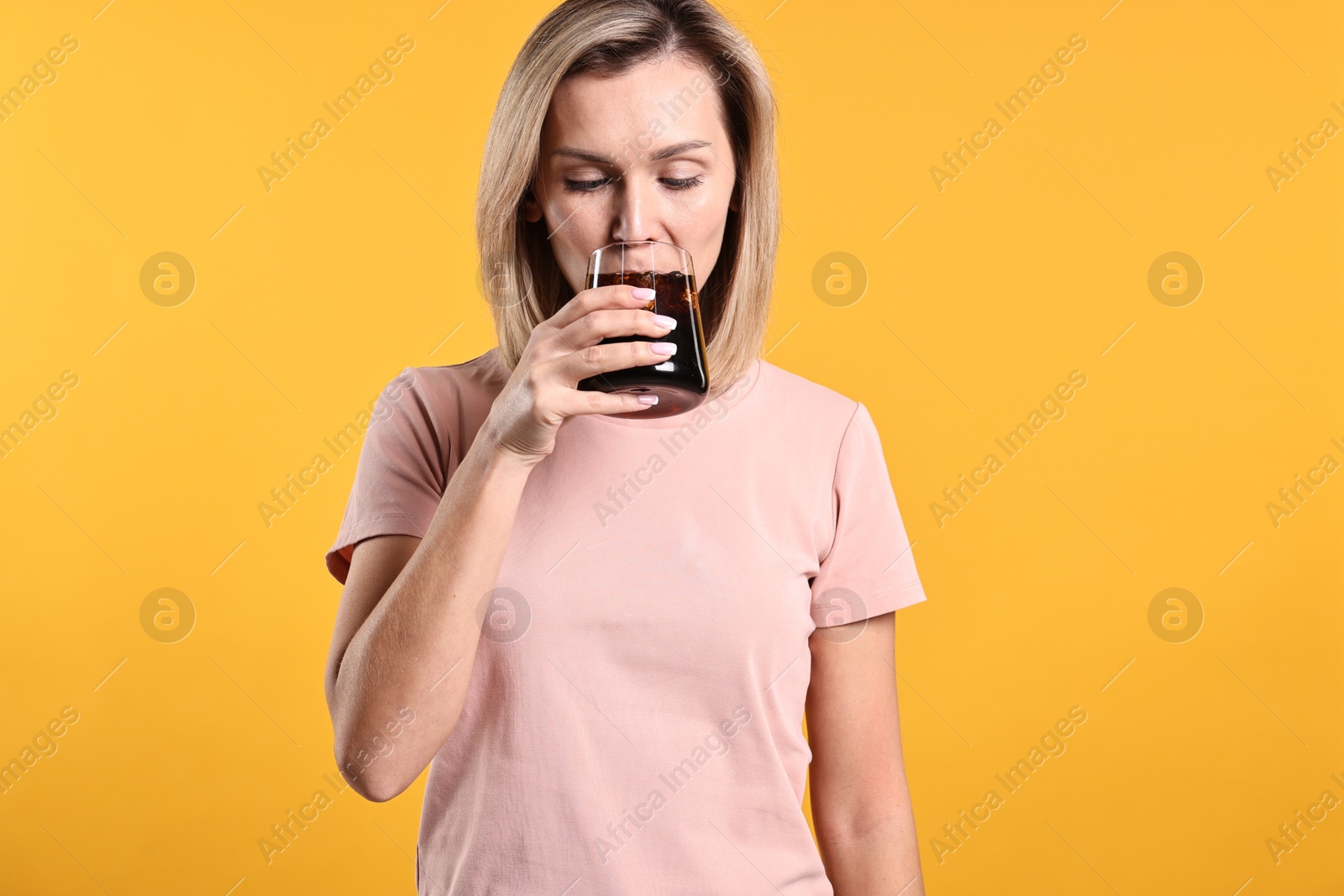 Photo of Woman drinking tasty refreshing soda drink on orange background.