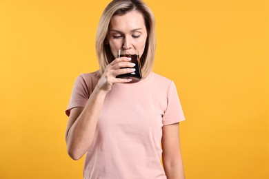 Photo of Woman drinking tasty refreshing soda drink on orange background.