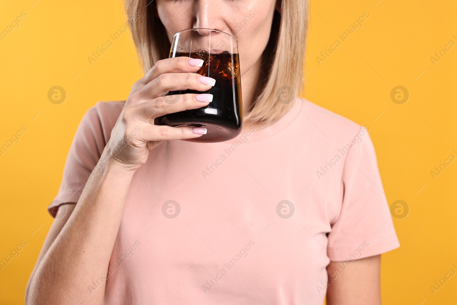 Photo of Woman drinking tasty refreshing soda drink on orange background, closeup