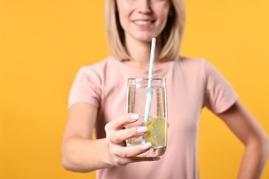 Photo of Woman with glass of lemonade on orange background, closeup. Refreshing drink