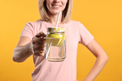 Photo of Woman with glass of lemonade on orange background, closeup. Refreshing drink