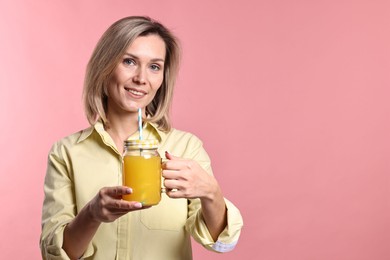 Photo of Woman with mason jar of orange juice on pink background. Refreshing drink