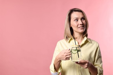 Woman with mason jar of lemonade on pink background. Refreshing drink