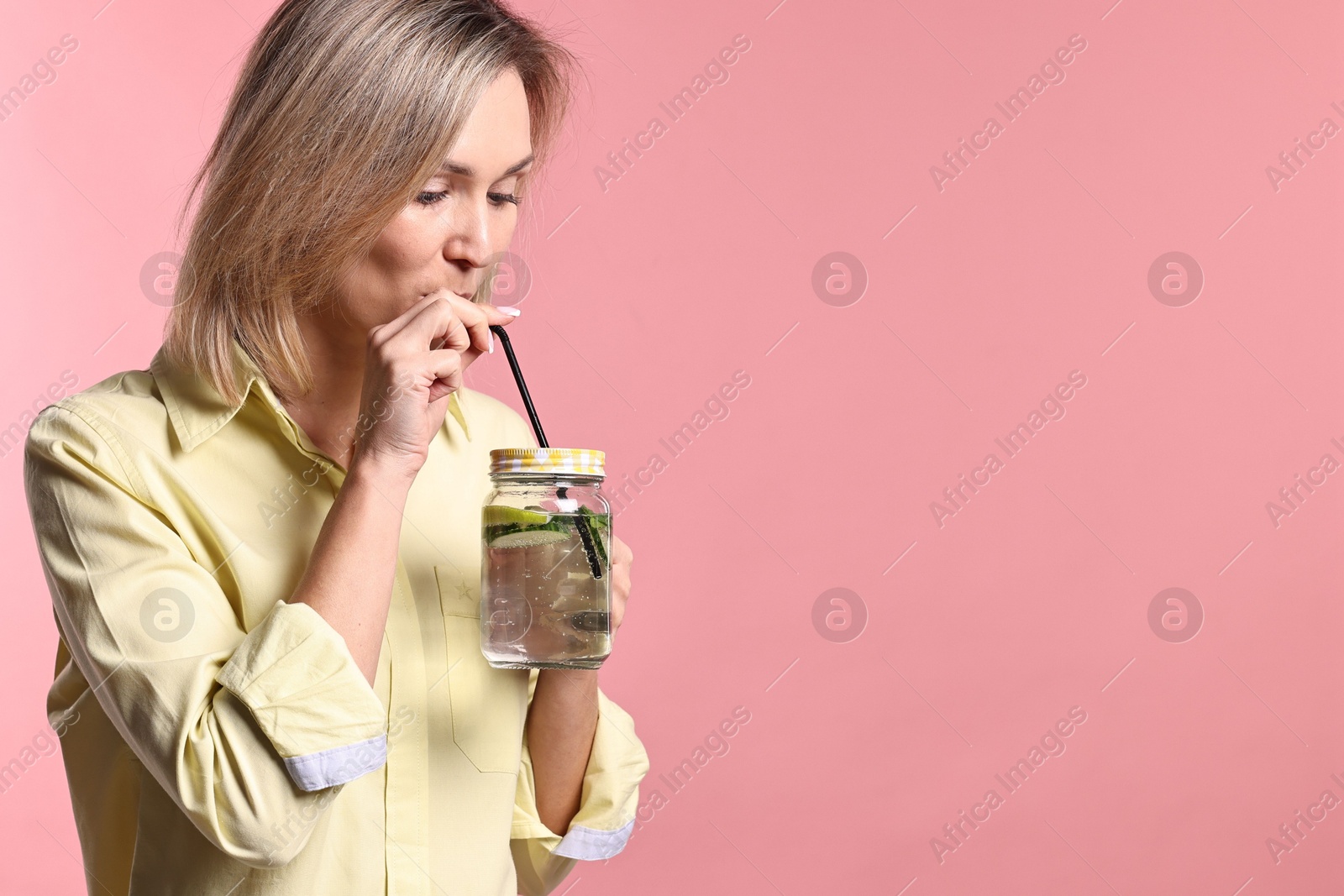 Photo of Woman drinking tasty lemonade on pink background. Refreshing drink