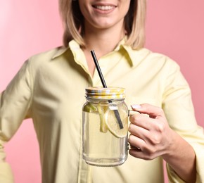 Photo of Woman with mason jar of lemonade on pink background, closeup. Refreshing drink