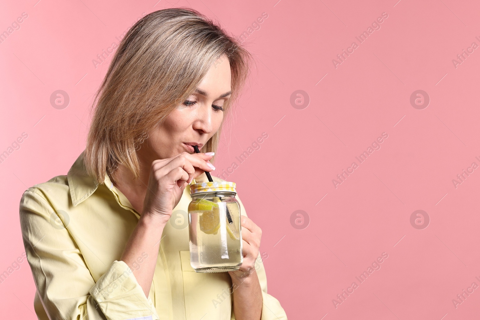 Photo of Woman drinking tasty lemonade on pink background, space for text. Refreshing drink