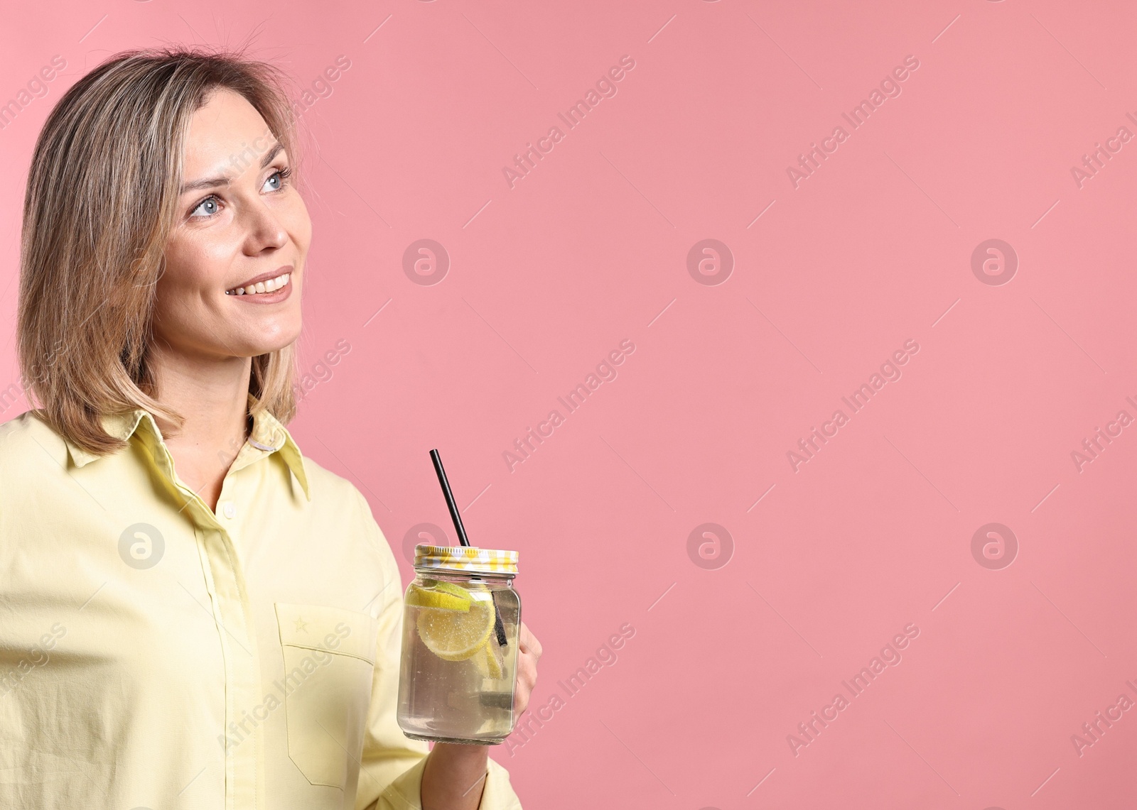 Photo of Woman with mason jar of lemonade on pink background. Refreshing drink