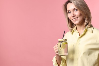 Photo of Woman with mason jar of lemonade on pink background, space for text. Refreshing drink