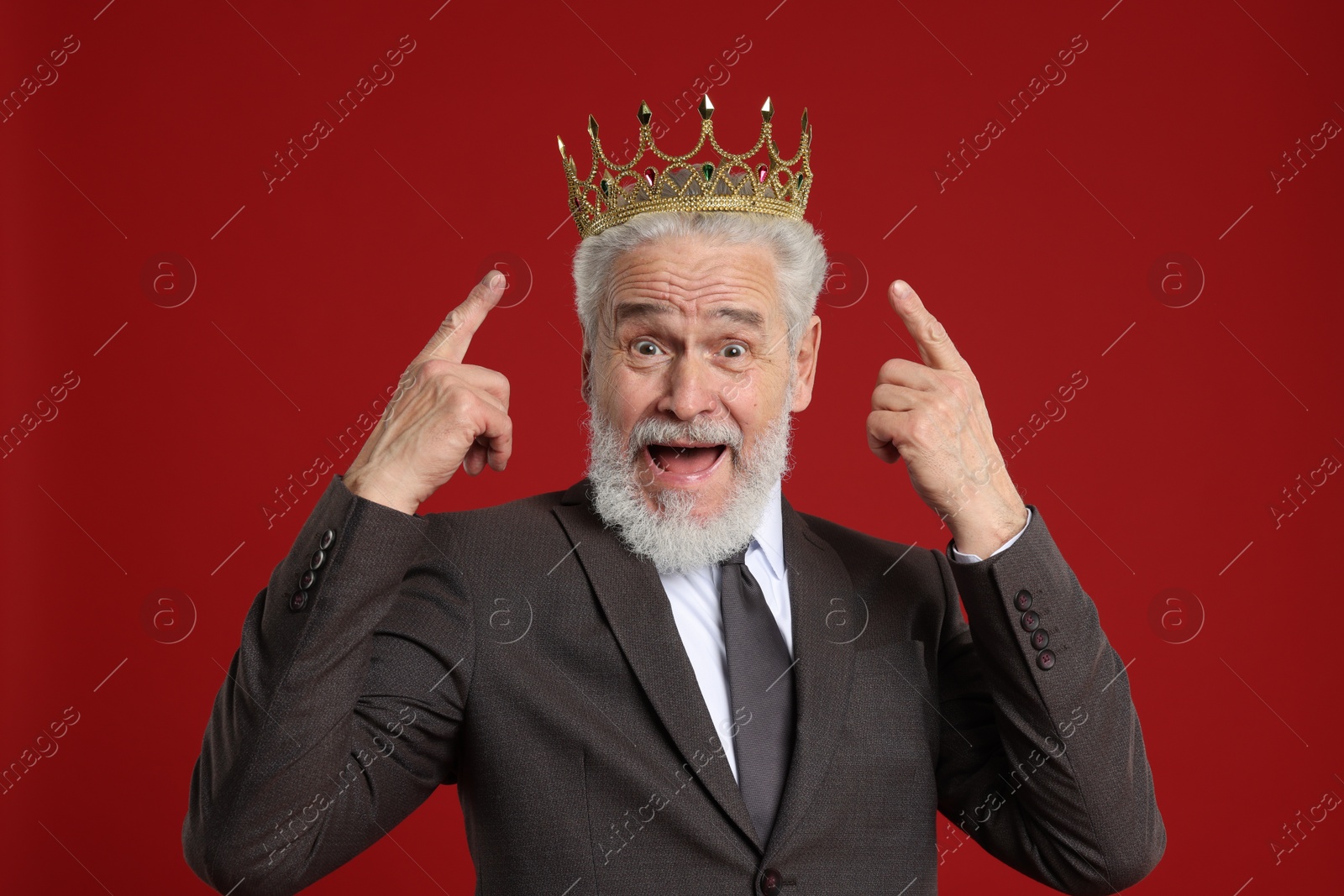 Photo of Senior man pointing at luxury crown on red background