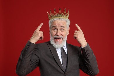 Photo of Senior man pointing at luxury crown on red background