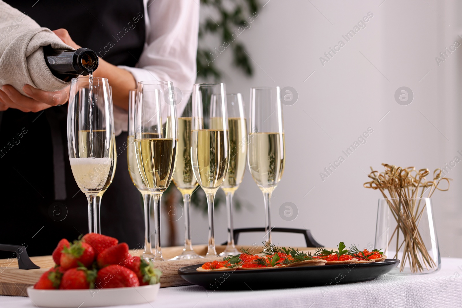 Photo of Waiter filling glasses with champagne indoors, closeup