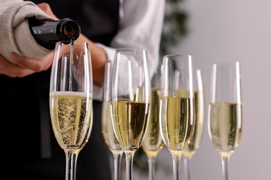 Photo of Waiter filling glasses with champagne indoors, closeup