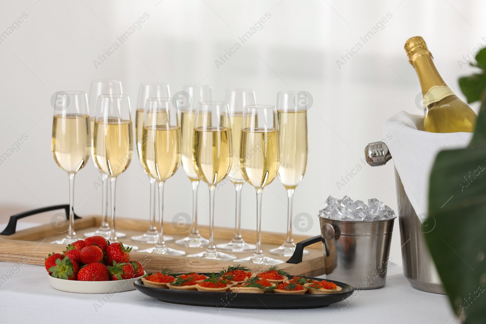 Photo of Champagne, ice bucket, strawberries and canapes with red caviar on white table indoors