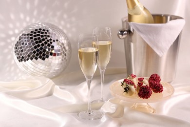 Photo of Champagne in glasses, ice bucket with bottle and tasty candies on white fabric