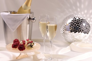 Photo of Champagne in glasses, ice bucket with bottle and tasty candies on white fabric